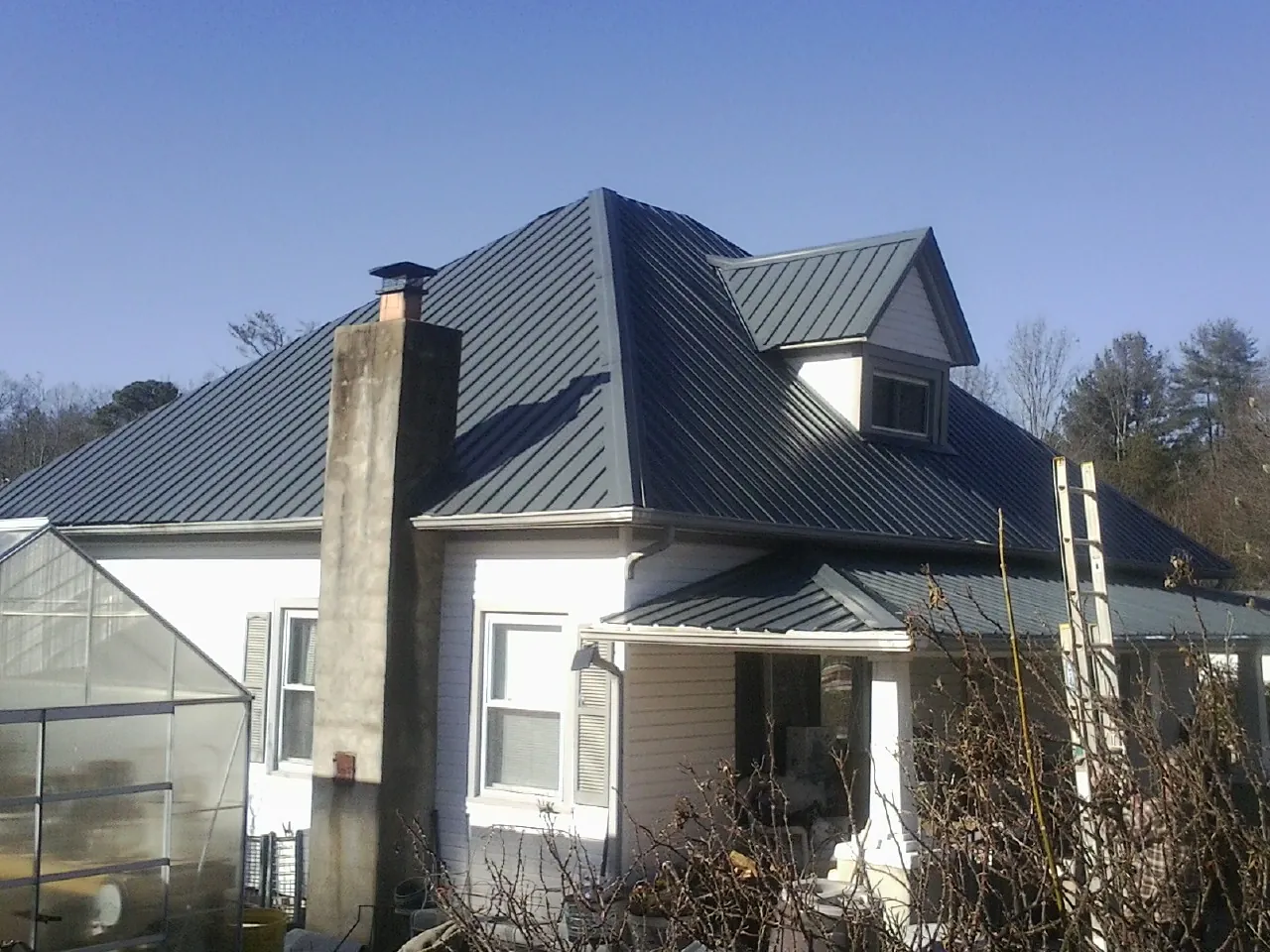 Dark blue standing seam metal roof on a white farmhouse with dormer — Slate & Tile Roof Repair by Roofing Brothers in Marble