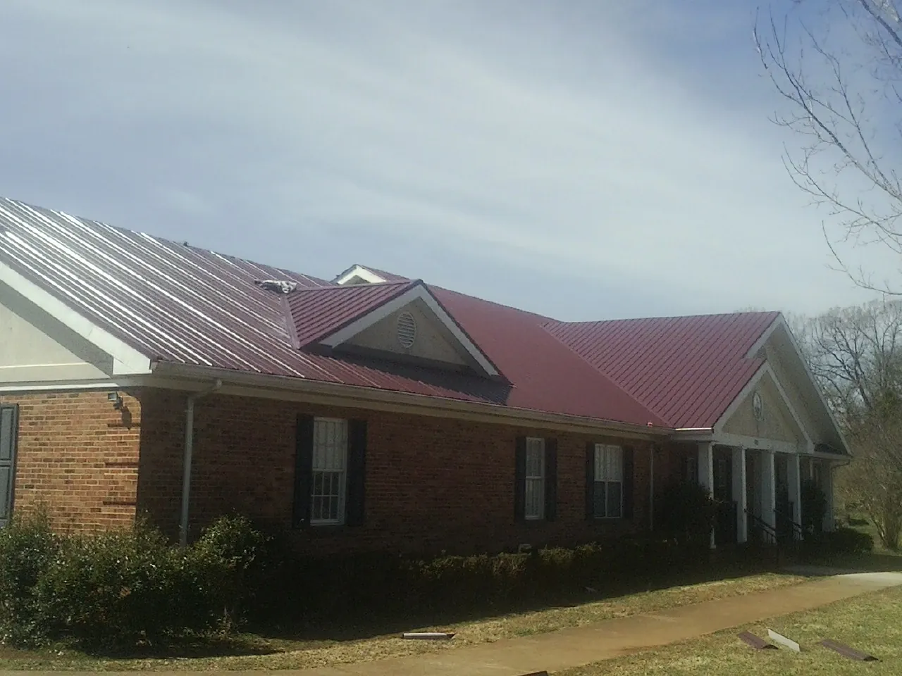 Red metal roof with gabled entries on a long brick building, from a Hail Damage Roof Repair job in Marble
