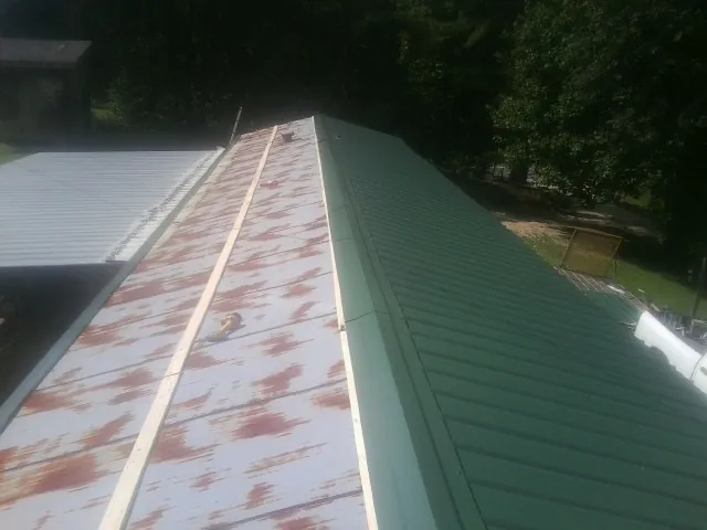 Old rusted panels beside newly installed green metal roofing — Wind Damage Roof Repair by Roofing Brothers in Marble