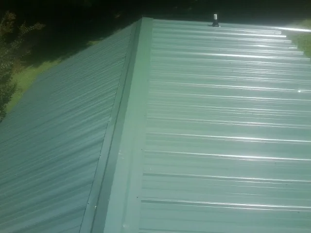 New green metal panels meeting at the ridge of a roof — Flat Roof Repair work by our crew in Marble