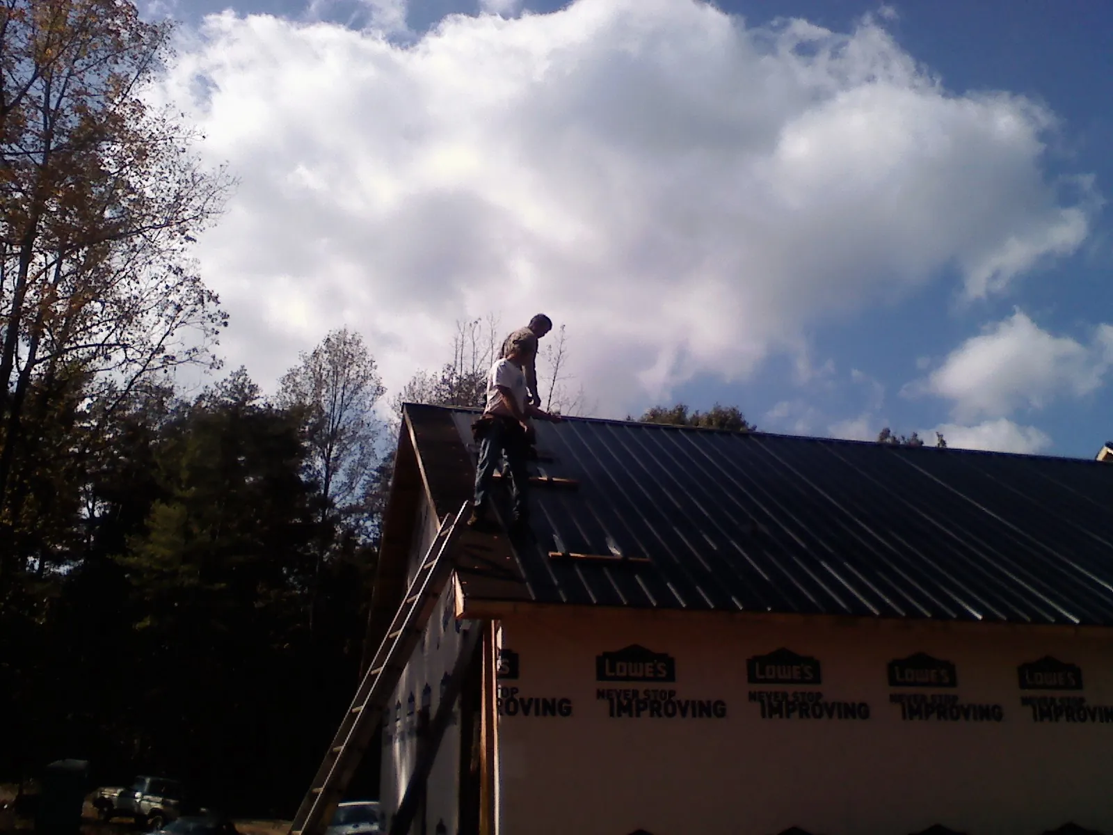 Roofer fastening dark metal panels high against a cloudy sky, from a Roof Inspection job in Marble