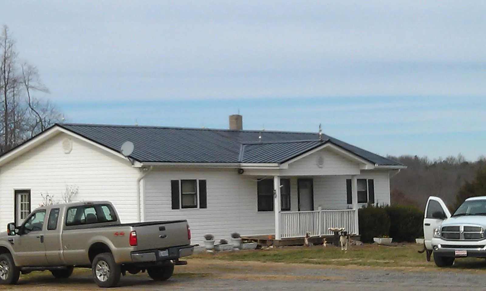 Finished dark metal roof on a white ranch home with work trucks parked in Marble